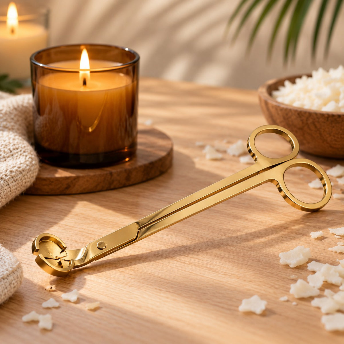 Tijeras cortamechas doradas para velas con vela encendida en vaso ámbar - Naturcera
