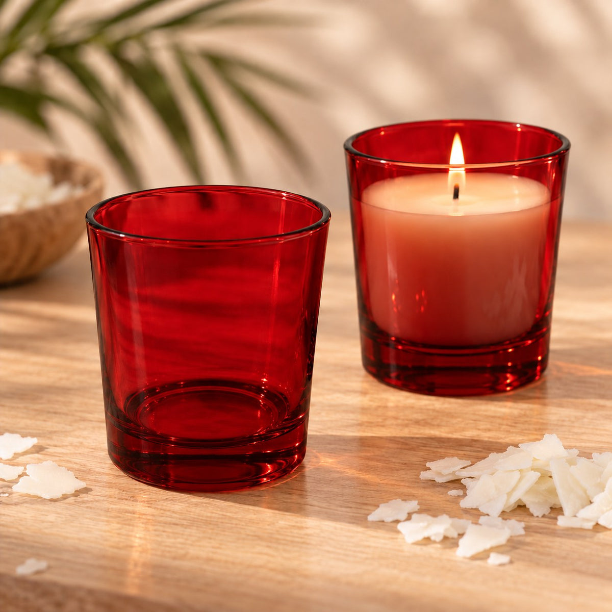 Bicchieri per candele in vetro rosso trasparente, uno vuoto e uno con candela di soia accesa