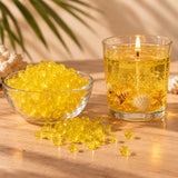 Perle di cera gel gialla per candele in una ciotola e candela gel gialla accesa con conchiglie