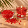 Perle di cera gel rossa per candele in una ciotola e candela gel rossa accesa con conchiglie