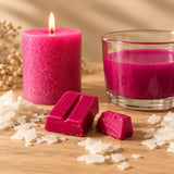 Blocchetti di colorante solido magenta per candele accanto a una candela a colonna e cera fusa colorata di magenta