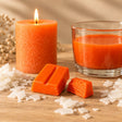 Blocchetti di colorante solido arancione per candele accanto a una candela a colonna e cera fusa colorata di arancione