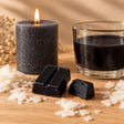Blocchetti di colorante solido nero per candele accanto a una candela a colonna e cera fusa colorata di nero