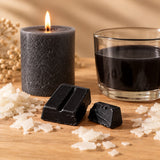 Blocchetti di colorante solido nero per candele accanto a una candela a colonna e cera fusa colorata di nero