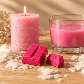 Blocchetti di colorante solido rosa per candele accanto a una candela a colonna e cera fusa colorata di rosa