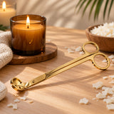 Tijeras cortamechas doradas para velas con vela encendida en vaso ámbar - Naturcera