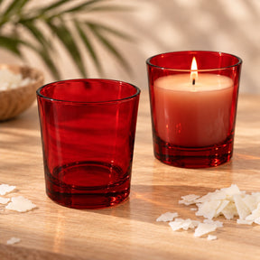 Bicchieri per candele in vetro rosso trasparente, uno vuoto e uno con candela di soia accesa