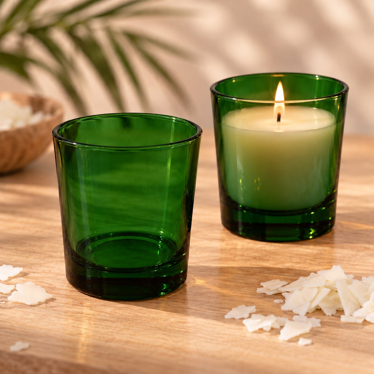 Bicchieri per candele in vetro verde trasparente, uno vuoto e uno con candela di soia accesa